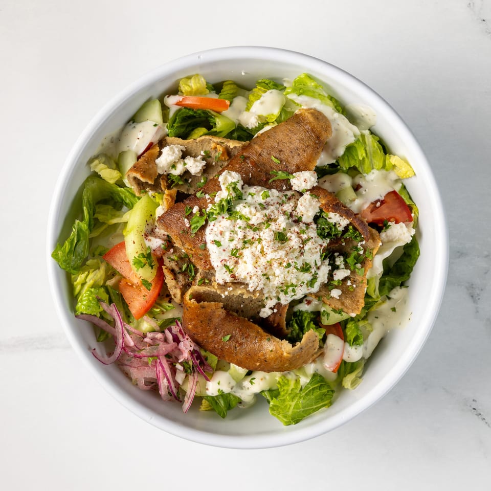 Mediterranean salad bowl topped with crispy pita, feta cheese, lettuce, tomatoes, cucumbers, onions, herbs, and creamy dressing.