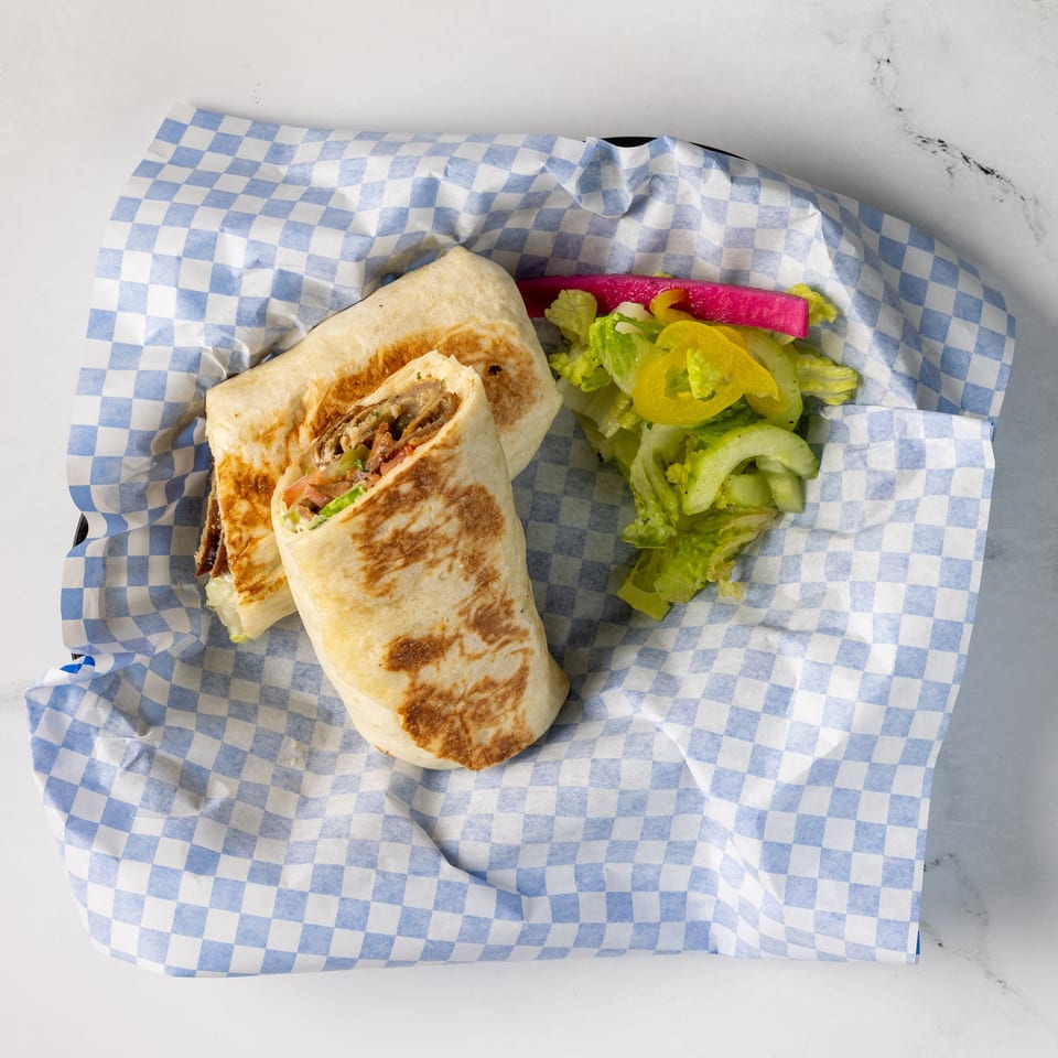 Grilled shawarma wrap cut open to reveal meat and vegetables, served with lettuce, cucumber, tomato, and pickled vegetables.