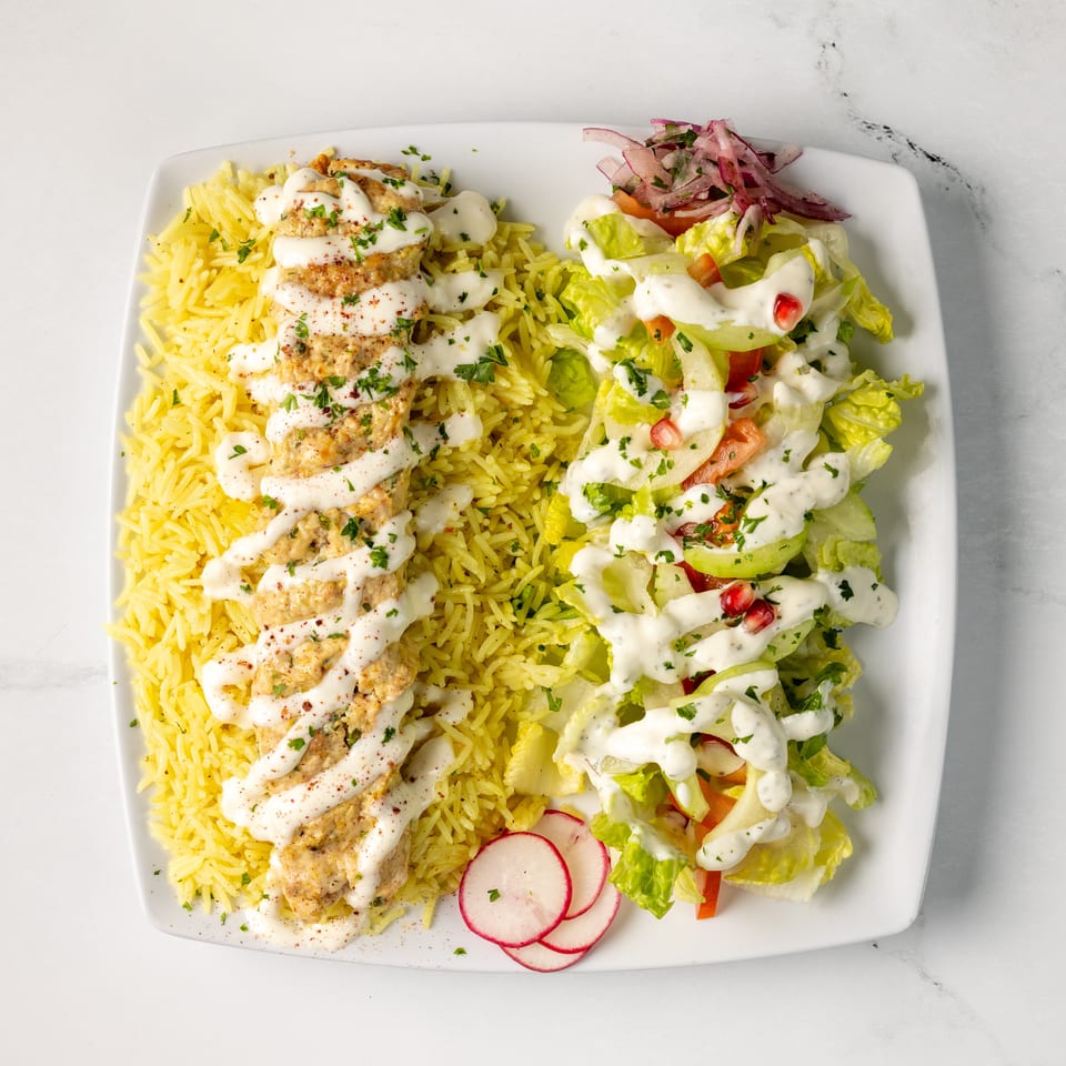 Mediterranean platter with grilled chicken, yellow rice, creamy sauce, fresh salad, pickled onions, and radishes.