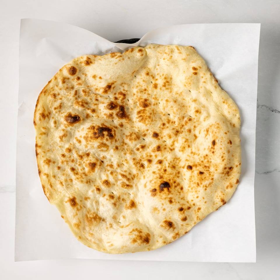 Large golden flatbread with browned spots rests on white parchment paper.