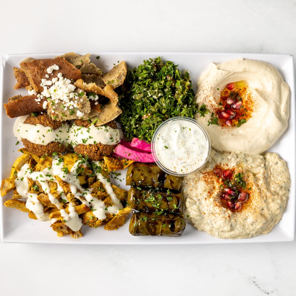 Mediterranean platter featuring falafel, shawarma, hummus, tabbouleh, stuffed grape leaves, pickled vegetables, and creamy sauces.