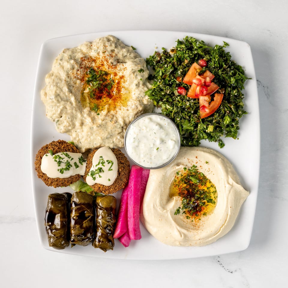 Mediterranean platter with hummus, baba ganoush, falafel, tabbouleh, stuffed grape leaves, pickled vegetables, and yogurt sauce.
